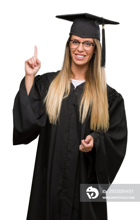 Beautiful young woman wearing glasses and graduation robe surprised with an idea or question pointing finger with happy face, number one