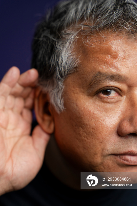 Portrait of serious man with hand on ear against purple background