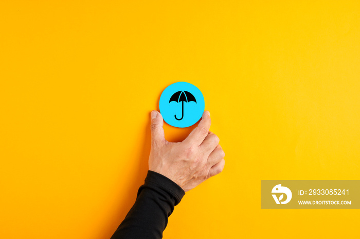 Male hand placing a blue badge with an umbrella icon representing insurance or protection.