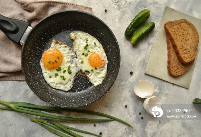 Tasty breakfast. Food on the table. Food on a light gray decorative background. Fried eggs in a pan. Eggs, green onions, brown bread, cucumbers.