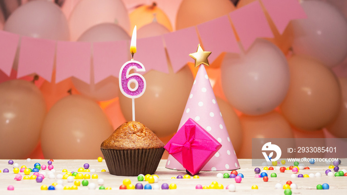 Decorations with balloons and a happy birthday candle with the number 6 years old for a child. Happy birthday greetings in pink colors for a six year old child for a girl, copy space. Muffin