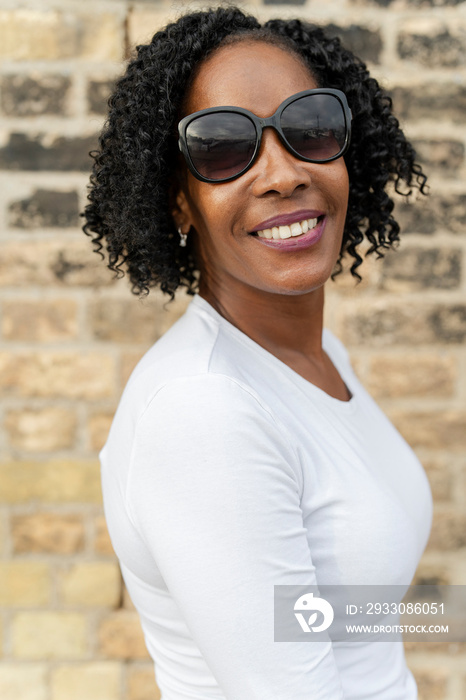 Portrait of smiling woman in sunglasses against brick wall