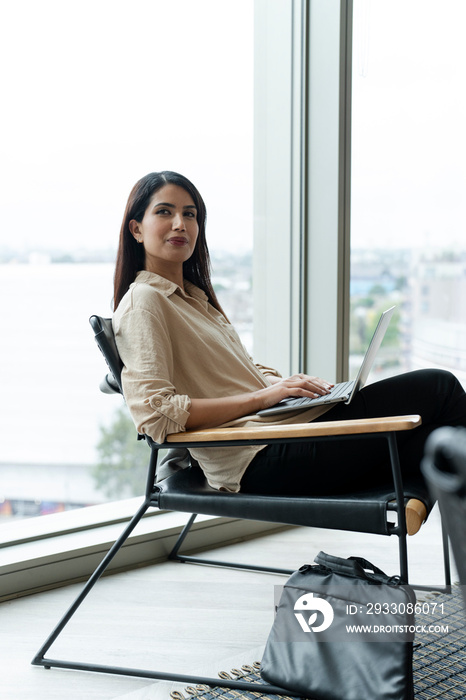 Businesswoman with laptop sitting in office lobby