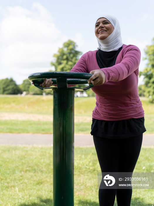 UK,Sutton,Smiling woman in headscarf exercising at park gym