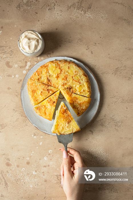 Female hand holding one portion of tortilla, spanisj  frying pan with tortilla,omelette made with eggs and potatoes.