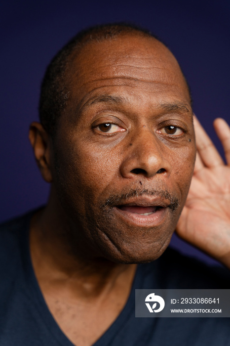 Portrait of man with hand on ear against purple background