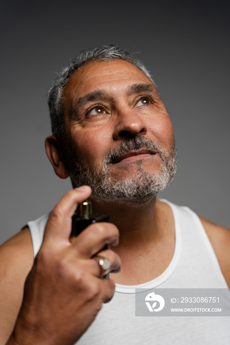 Portrait of man putting on perfume against gray background