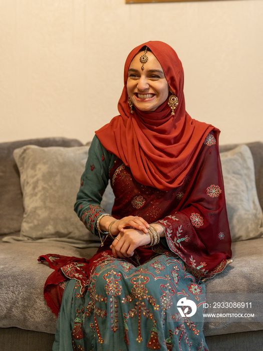 Smiling woman wearing hijab sitting on sofa