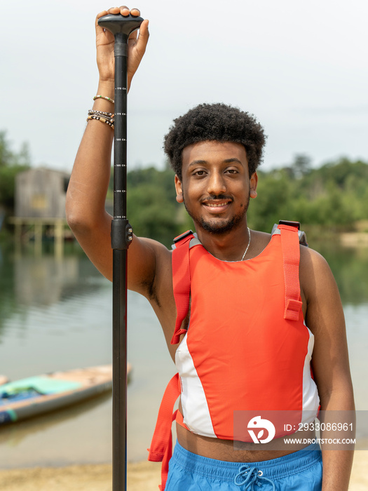 Portrait of young man standing with oar on beach
