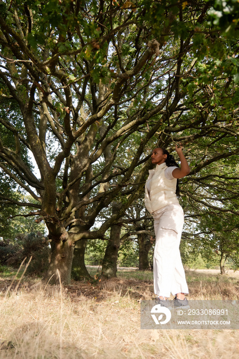 Young woman standing under tree in grassy field