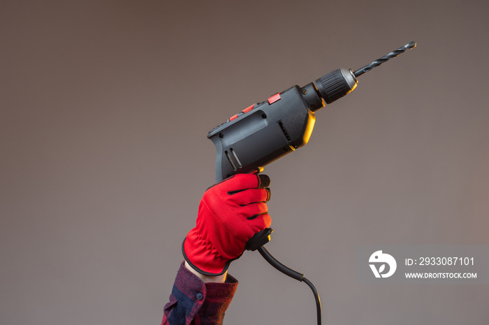 Hand with an electric drill. Construction electric tool. Hands in construction gloves. Electric drill on a dark background. Concept - drilling holes. Concept - sale of drills for construction.