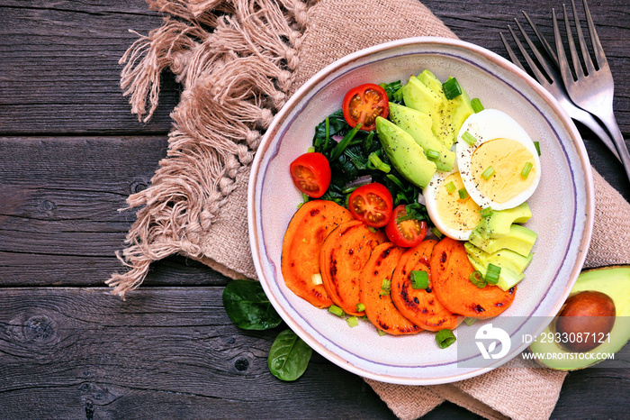 Breakfast nutrient bowl with sweet potato, egg, avocado and spinach. Overhead view table scene on a rustic wood background.