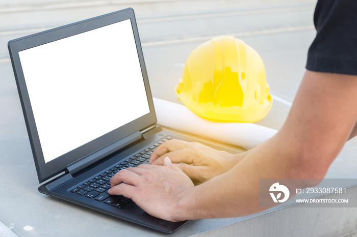 The human hands typing a keyboard on laptop with white screen isolated at construction site with yellow helmet background