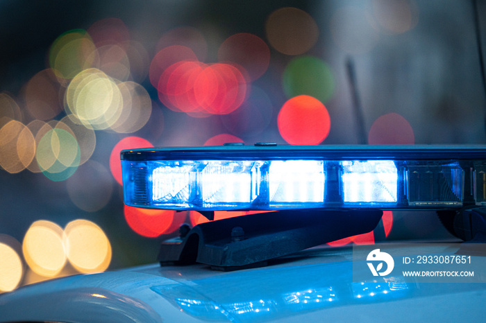 Blue lights on the roof of a police car with the background out of focus and lights with bokeh effect