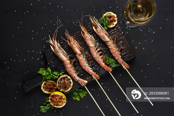 Grilled shrimp skewers. Seafood, shellfish. Shrimps Prawns skewers with herbs, garlic and lemon on black stone background, copy space.