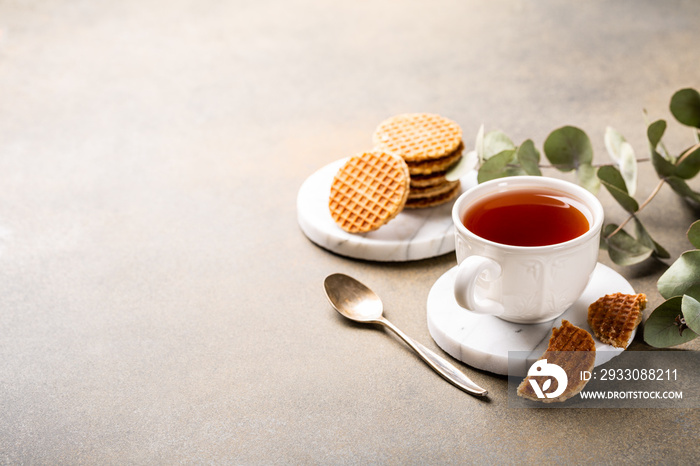 Cup of tea with mini stroopwafel, syrupwaffles cookies and eucalyptus twigs on light background with copy space.