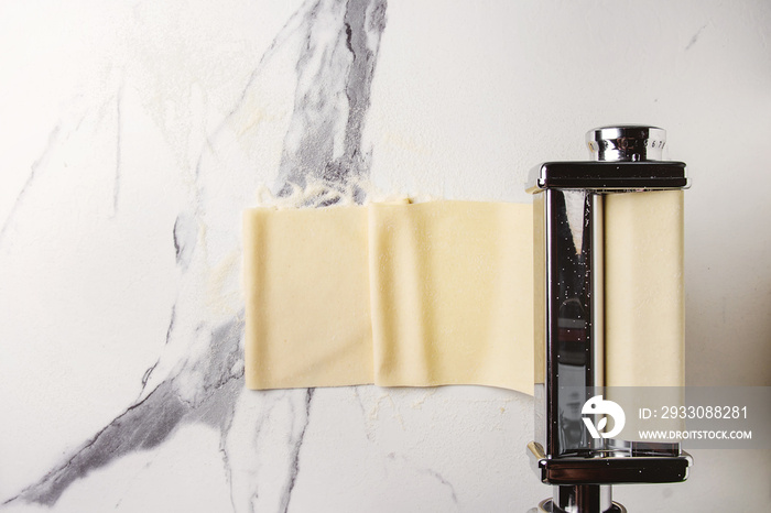 Rolled dough for homemade italian uncooked pasta lasagna from pasta machine maker with semolina flour over white marble texture background. Flat lay, space.