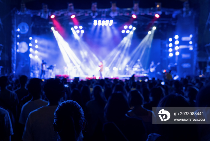 Silhouettes of crowd, group of people, cheering in live music concert in front of colorful stage lights.