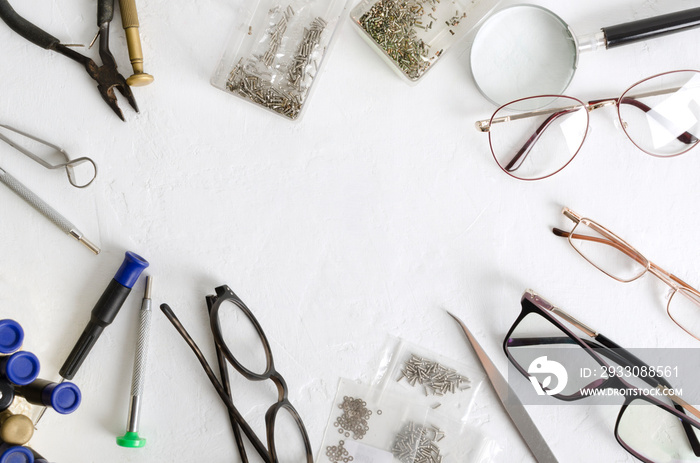 Top view of optical screws, screwdrivers, lens, eyeglasses and different professional tools for glasses fixing on the white table.Empty space