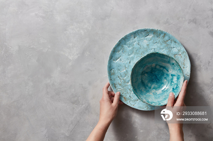 Vintage painted glazed plates dishes on gray concrete table with free space ror text. Girl hold handcraft bowl in her hand. .