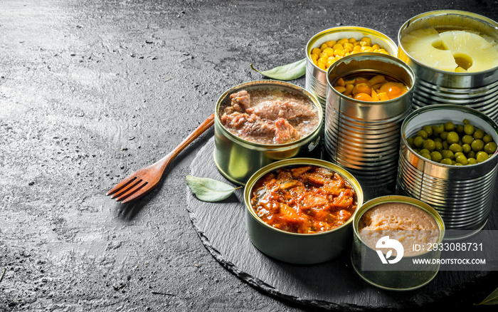 Various open tin cans of canned food on a stone Board with a fork.