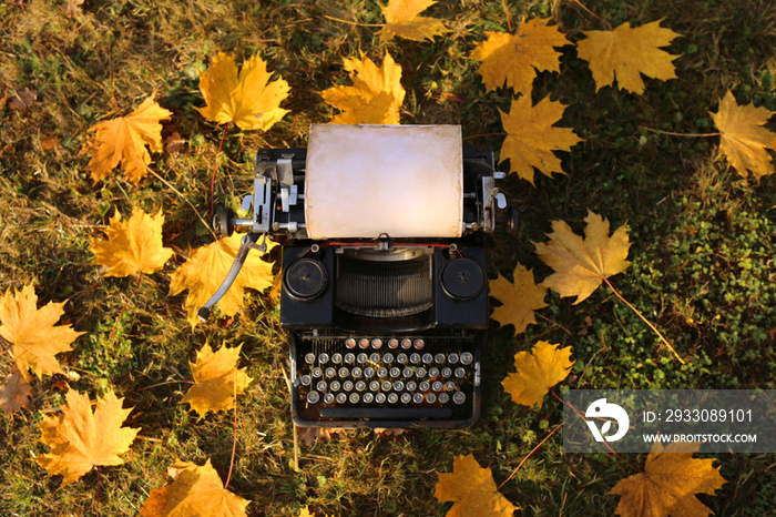 Autumn. World Book Day.  Autumn Writing Marathon.NaNoWriMo.  Black retro typewriter and yellow maple leaves in the grass.Fall time.Autumn cozy mood.	 writing marophon