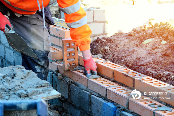 Industrial bricklayer laying bricks on cement mix on construction site. Fighting housing crisis by building more affordable houses concept