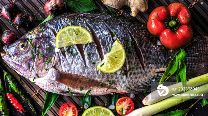 Top view delicious fresh fish and herbs and spices, lemon, tomato, chili and various vegetables on dark wood background, space for texture. Healthy food, diet or cooking concept.