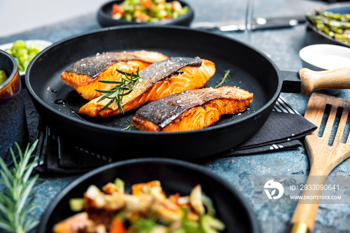 Gebratener Lachs serviert in einer Pfanne mit Beilagen Salat.