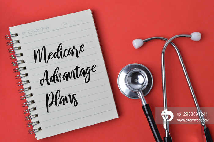 Top view of stethoscope and notebook written with text MEDICARE ADVANTAGE PLANS over red background.