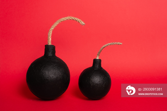 Photo of a round bomb with lit fuse on a red background. Big bomb and small bomb on red background.