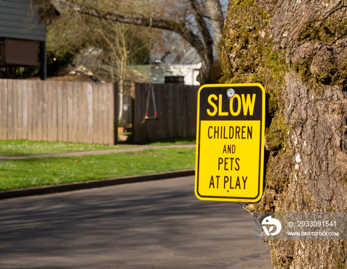 A black and yellow sign reading, Slow Children and Pets at Play posted on a tree