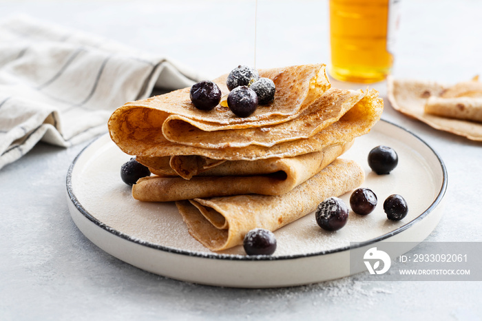 Freshly baked thin pancakes, crepes with blueberries and honey on blue plate. Healthy breakfast. Gray background