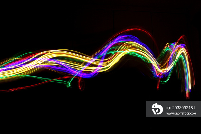 Long exposure photograph of neon multi colour in an abstract swirl, parallel lines pattern against a black background. Light painting photography.