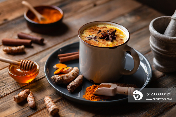 Golden milk in white mug, turmeric latte made with curcuma, cinnamon, anise, honey. Healthy hot winter drink, natural, organic beverage. Close up, front view.  Wooden rustic background