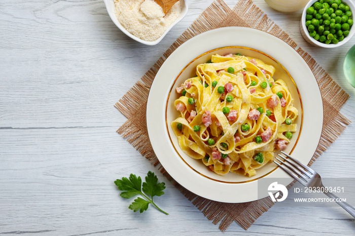 Italian Traditional Dish Tagliatelle panna,piselli e pancetta ,tagliatelle pasta with heavy cream,peas,smoked bacon,olive oil,onion,parmesan cheeses and peppers on plate with white wood background