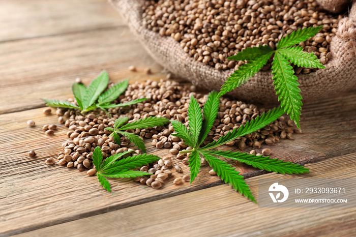 Heap of hemp seeds in bag on wooden background