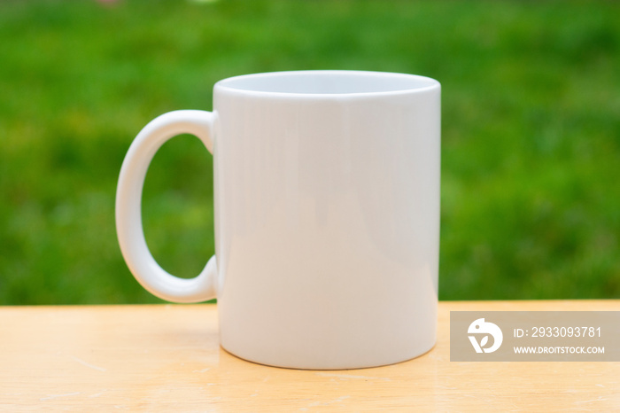 White porcelain mug cup isolated on green grass background with copy space. Coffee or tea cup.