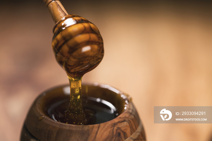 honey drips from dipper into wooden pot