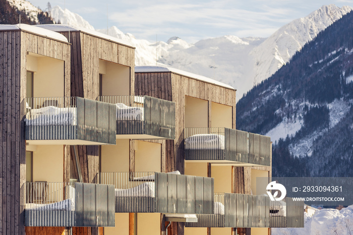 Wooden, mountain house located on the background of snowy mountains and forests. Large balconies covered with snow halfway.