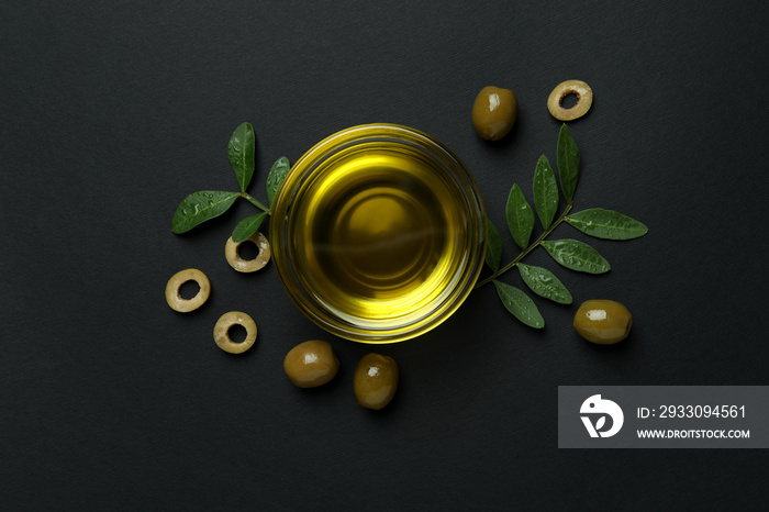 Bowl of oil, olives and twigs on black background