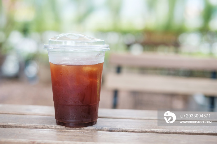 Iced americano coffee cup on wooden table against nature background at cafe