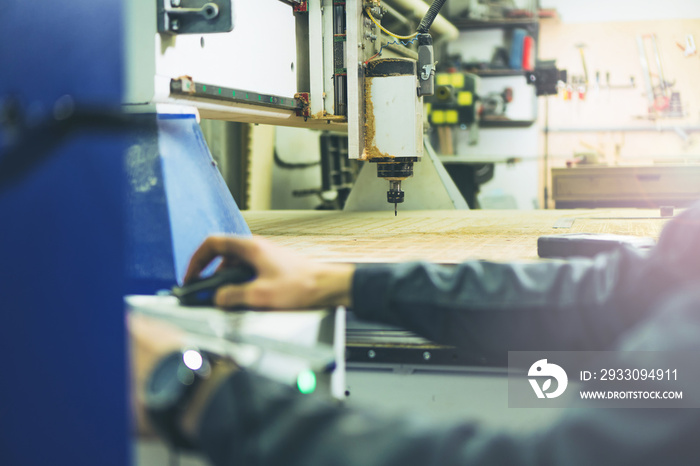 Engineer making settings on remote control of CNC wood milling machine for cutting wood