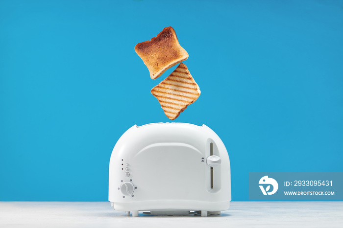 Roasted toast bread popping up of toaster with blue wall, front view