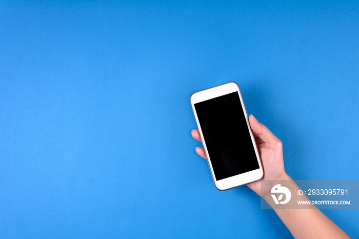 Hand touching smartphone screen on blue background. Mock-up. Top view. Copy space