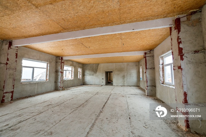 Unfinished apartment or house big loft room under reconstruction. Plywood ceiling, plastered walls, window openings, cement floor. Construction and renovation concept.