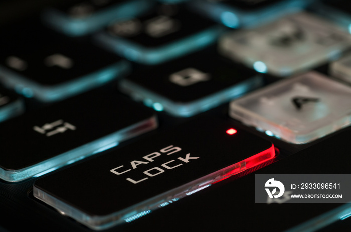 The Caps lock key on a backlit keyboard. The red illuminated dot on the key indicates that the capslock is turned on. Closeup, selective focus.