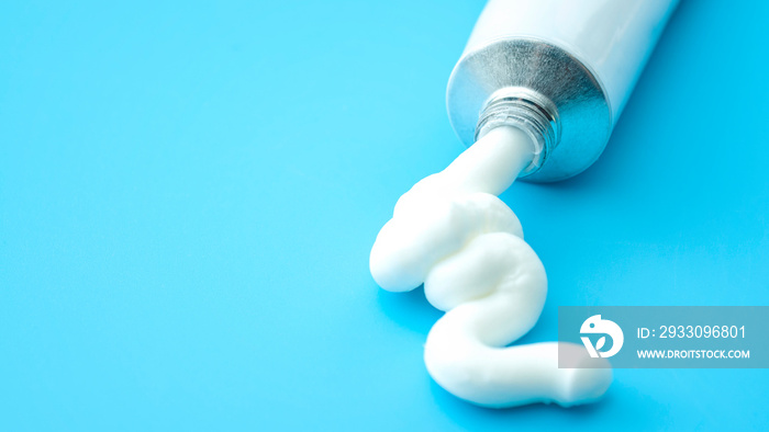 Dermatology, pharmaceutical medicine or healing topical application ointment concept with metal tube pushing white cream isolated on blue background with copy space