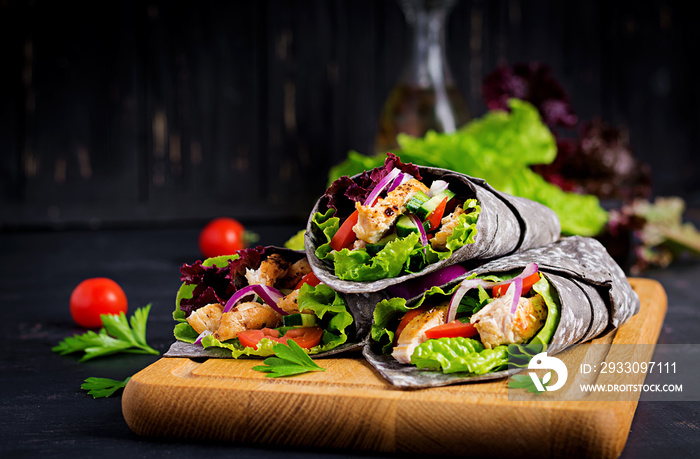 Tortilla with added ink cuttlefish wraps with chicken and vegetables on black background. Chicken burrito, mexican food.