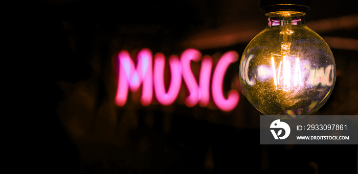 Electric incandescent lamp on the background of half-blurred neon music inscription.